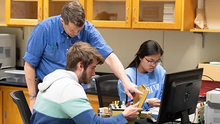 Professor working with students in an electronics lab.